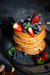 Pile of pancakes with blueberries and strawberries on a plate with dark background  