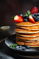Pile of pancakes with blueberries and strawberries on a plate with dark background  
