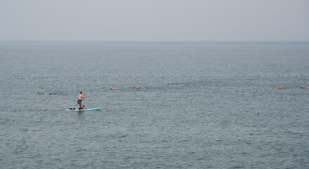 Fototapeta na wymiar Unrecognized person canoeing in the sea in the morning with dogs. People exercising in the ocean.