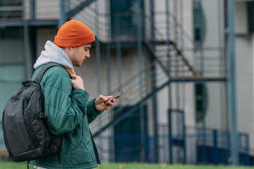 young man or student with backpack on the street looking at his mobile phone