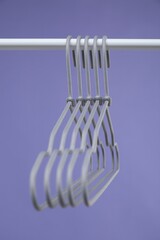 Empty clothes hangers on rack against purple background, closeup