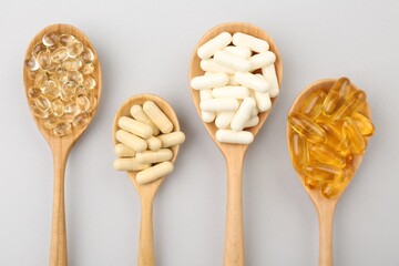 Wooden spoons with different vitamin capsules on light grey background, flat lay