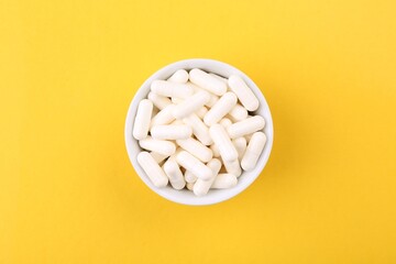 Vitamin capsules in bowl on orange background, top view