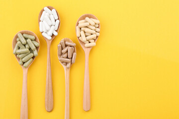 Different vitamin capsules in wooden spoons on yellow background, flat lay. Space for text