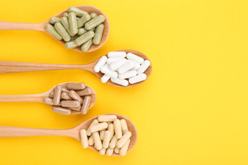 Different vitamin capsules in wooden spoons on yellow background, flat lay. Space for text