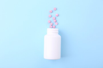 Jar with vitamin pills on light blue background, top view