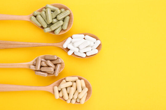 Different vitamin capsules in wooden spoons on yellow background, flat lay. Space for text