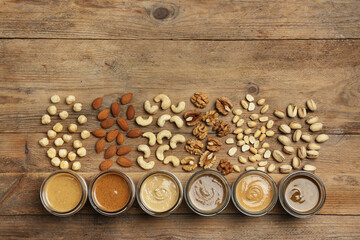 Nut butters in bowls and ingredients on wooden table, flat lay