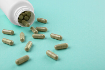 Bottle and vitamin capsules on turquoise background, closeup. Space for text