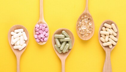 Different vitamin pills in wooden spoons on yellow background, flat lay