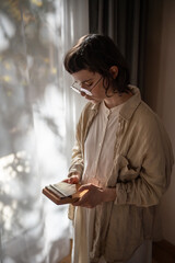 Teen girl studying to play music on kalimba standing near window at home. Girl relaxes plays on...