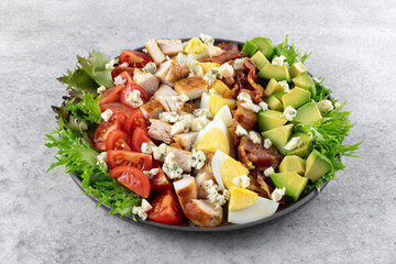 Classic American Cobb salad with tomatoes, bacon, chicken, eggs, avocado and blue cheese on a gray background. Top view. Copy space.
