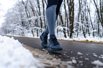 Closeup image of a person walking on wet road, snow on the ground and sports equipment in focus.