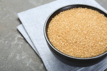 Brown sugar in bowl on grey textured table, closeup. Space for text