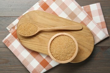 Brown sugar in bowl and spoon on wooden table, top view