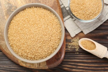 Brown sugar in bowls and scoop on wooden table, flat lay