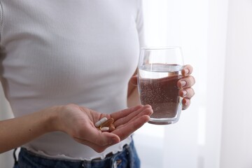 Woman with vitamin pills and glass of water indoors, closeup