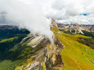 White heavy clouds descend covering Seceda bare peaks of mountain range. Scenic Italian Alps and...