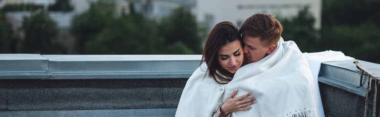 Beautiful young loving couple on a surprise romantic date on a roof top. Picturesque view, skyscrapers on background. Wine, candles, kisses on holiday Saint Valentine's Day celebration outdoors - Powered by Adobe
