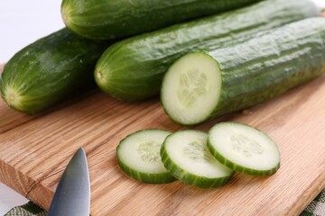 Fresh cucumbers and knife on wooden cutting board, closeup