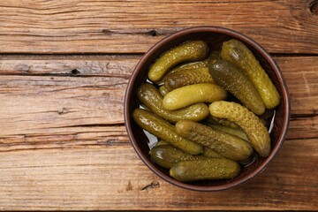 Tasty pickled cucumbers in bowl on wooden table, top view. Space or text
