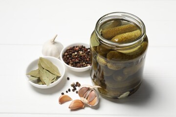 Tasty pickled cucumbers in jar and ingredients on white wooden table