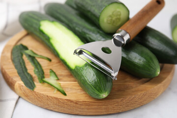 Fresh cucumbers and peeler on white table, closeup