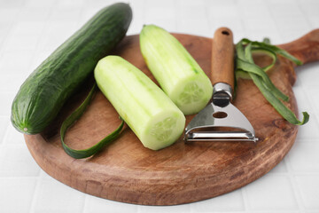 Fresh cucumbers and peeler on white tiled table, closeup