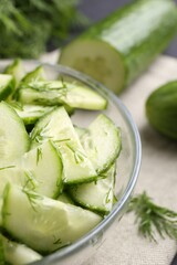 Cut cucumber with dill in glass bowl on table, closeup