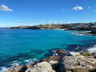 Bay and coastline close to the ocean. View of the city in the distance. Turquoise waves breaking on the rocky shore. Australia, NSW, landscape.