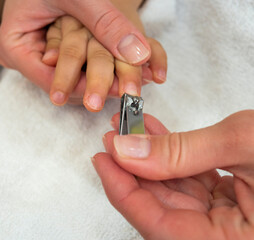 Caucasian young mother cuts baby's fingernails with special children's scissors, close up shot. Manicure for child.