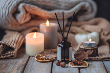Concept of house decor, apartment seasonal fragrance. Thanksgiving. Autumn mood, cozy fall home atmosphere. Aroma diffuser, pumpkins, knitted warm sweaters, burning candles, dry leaves on wooden table