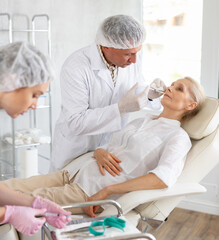 Professional cosmetic surgeon making face contouring injections to elderly female patient in...
