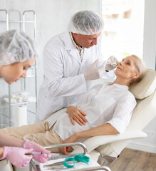 Professional cosmetic surgeon making face contouring injections to elderly female patient in cosmetology clinic, performing lip fillers..