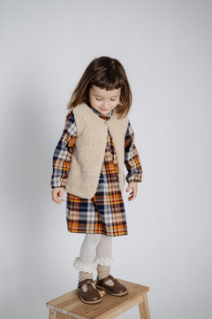 a small model poses for advertising photos of vintage children's dresses. A girl in a warm dress and a woolen vest with positive emotions