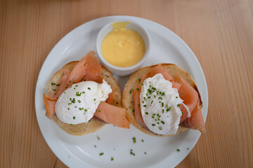 Two poached eggs on smoked salmon and an english muffin. A small dish of hollandaise sauce is on the side. - 724233529