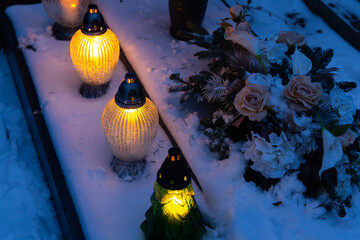 Candles burning at night on graves covered with snow. View of the cemetery on a winter evening
