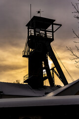 A mine hoist shaft against a dramatic sky background. Close up of the wheels at the top of the shaft.