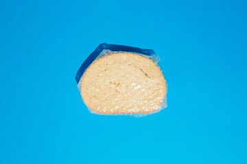 Top view of slice of fresh white bread with sesame seeds wrapped in foil against blue background. Bakery concept