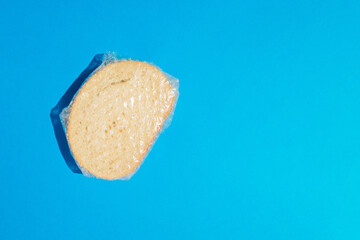 Top view of slice of fresh white bread with sesame seeds wrapped in foil against blue background. Copy space