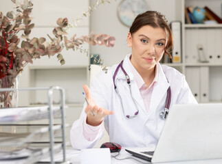 Positive woman doctor sitting at workplace with computer in her office