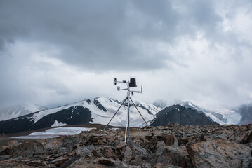 Automatic meteorological station on stone hill with view to large snow-capped mountain range....