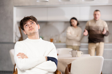 Fototapeta premium Young man relatives are unhappy with his behavior and scold him in the home kitchen
