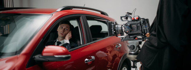 Professional male actor works in the frame on the set. Shooting with a car on a large white...
