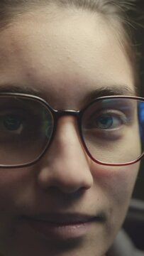 Vertical closeup slow motion portrait with software program reflecting in eyeglasses on young Caucasian female IT specialist looking at camera working at night