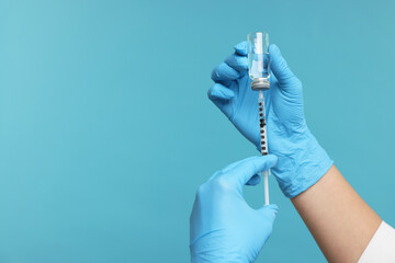 Doctor filling syringe with medication from glass vial on light blue background, closeup. Space for...