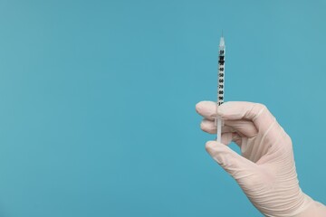 Doctor holding syringe on light blue background, closeup. Space for text