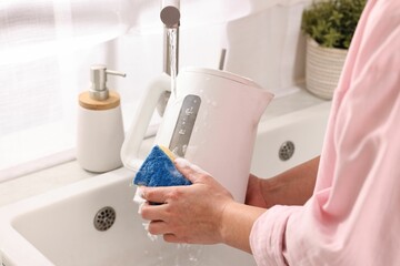 Woman washing electric kettle with sponge at sink in kitchen, closeup