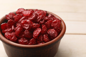 Tasty dried cranberries in bowl on light wooden table, closeup