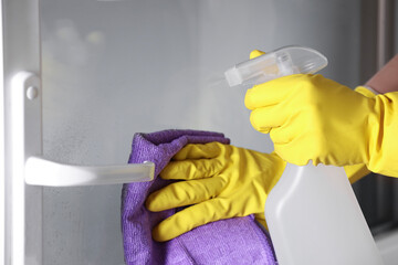 Woman with spray bottle and microfiber cloth cleaning window, closeup